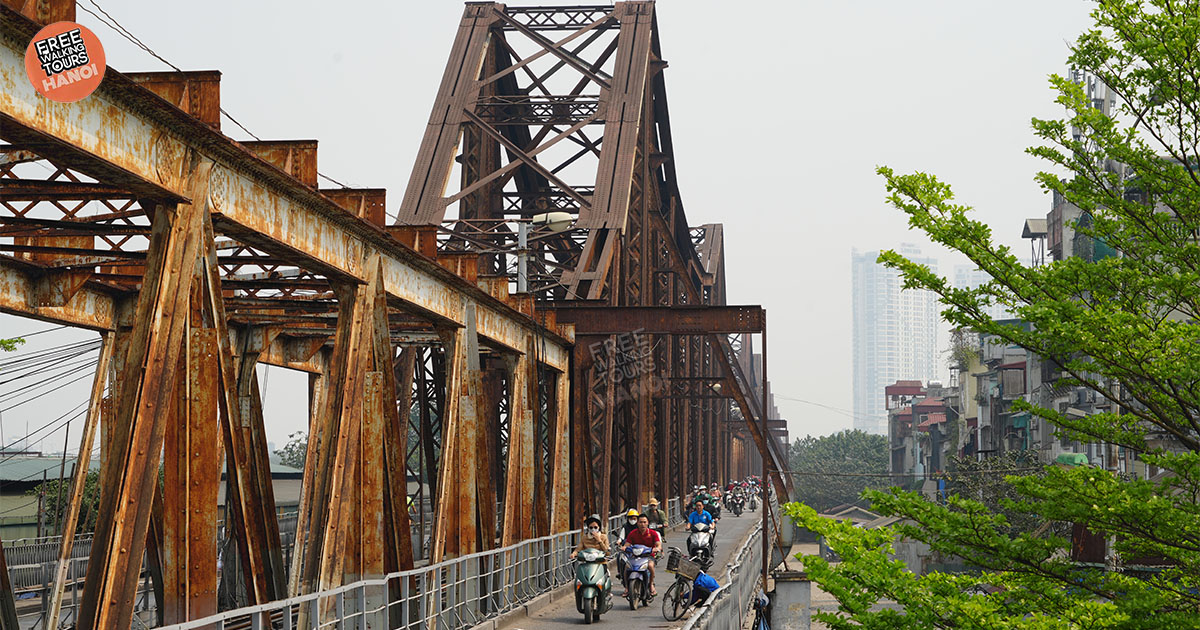Tourists walking on Long Bien Bridge at sunset with Red River view